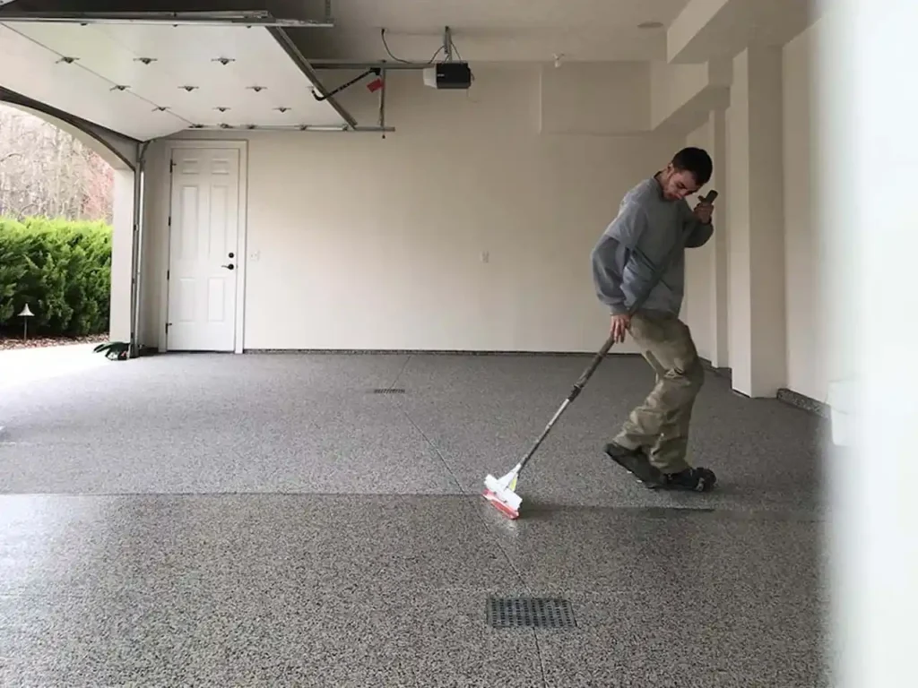 Person cleaning concrete garage floor with scrub brush and cleaner